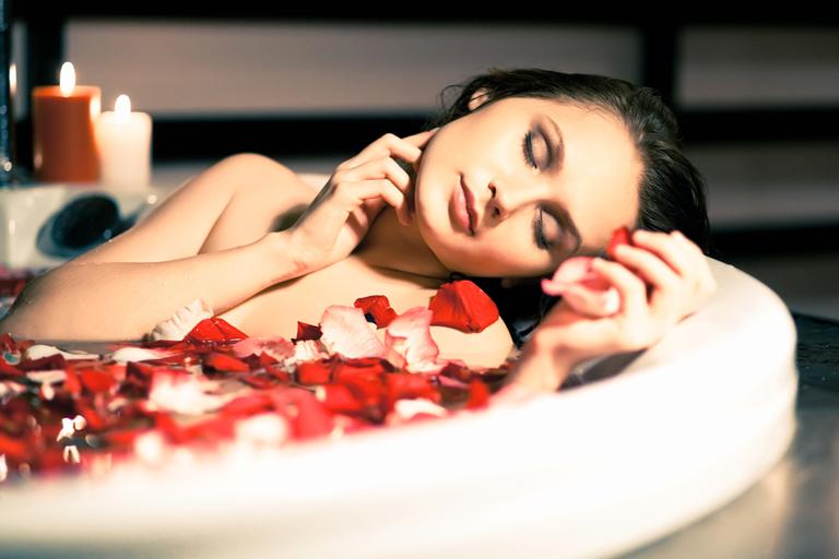 Mulher numa banheira com água e pétalas de rosa vermelhas.
