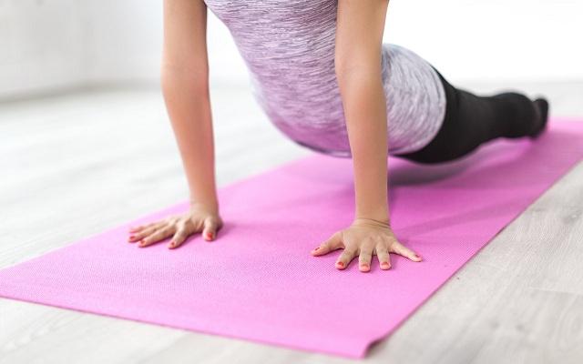 Na imagem, a mulher faz yoga em um tapete rosa. Incontinência urinária.