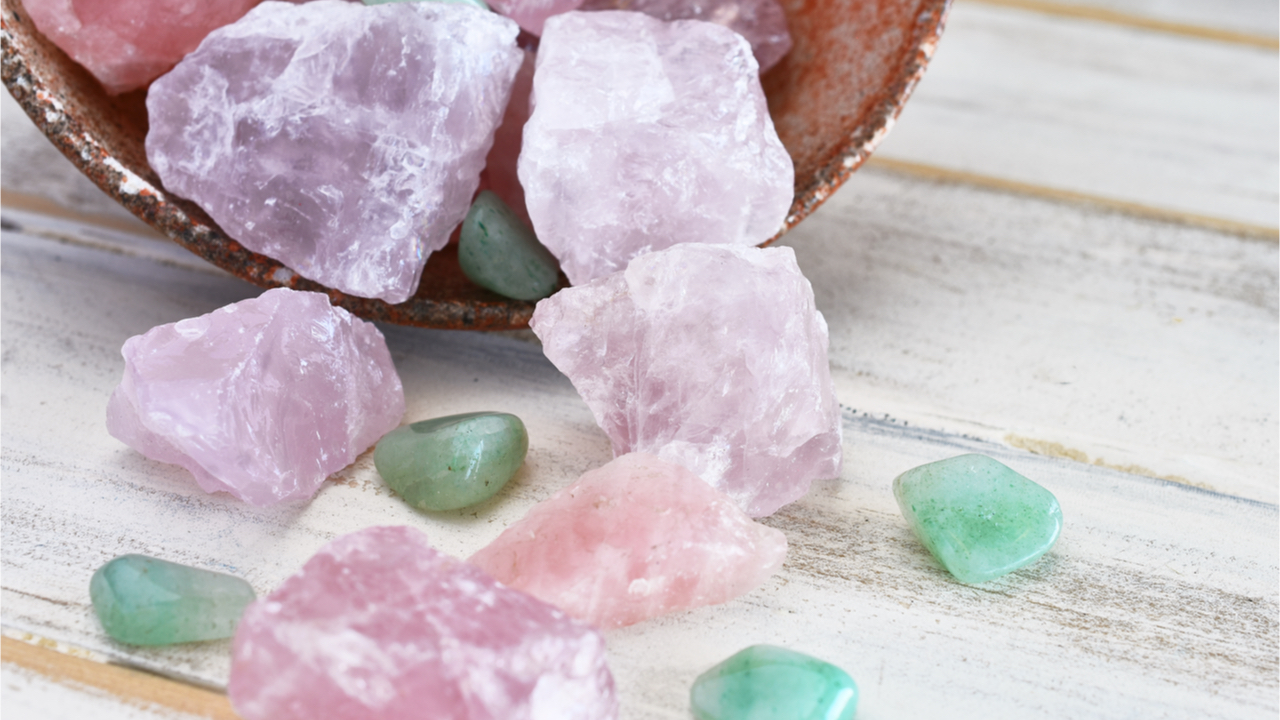 Uma imagem de perto de uma tigela de cerâmica inclinada, cheia de quartzo rosa e cristais de aventurina verde.