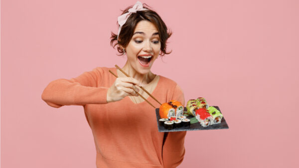 mulher segurando um prato de comida japonesa em fundo rosa