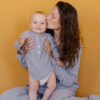 Mãe de pijama cinza beijando seu bebê. Mãe e filho. Alegria da maternidade. Cuidados de infância feliz. Fundo laranja.