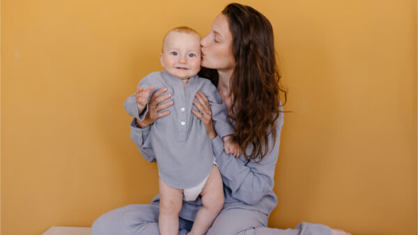 Mãe de pijama cinza beijando seu bebê. Mãe e filho. Alegria da maternidade. Cuidados de infância feliz. Fundo laranja.