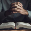 Homem com mão de oração e Bíblia no quarto escuro.