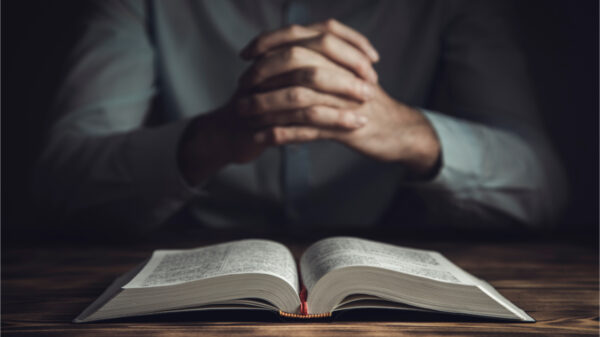 Homem com mão de oração e Bíblia no quarto escuro.