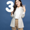 Jovem mulher mostrando o número 3 e apontando para cima com o dedo em número 3, isolada em fundo azul.