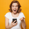 Retrato de uma garota feliz isolada sobre fundo laranja, usando telefone celular, comemorando.