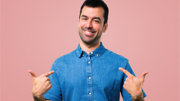 Homem com camisa azul orgulhoso e auto-satisfeito em fundo rosa.