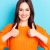 Foto de uma mulher alegre mostrando polegares para cima, sorrindo isolada no fundo de cor azul.