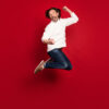 Foto do tamanho do corpo inteiro de um homem pulando isolado em fundo de cor vermelha.
