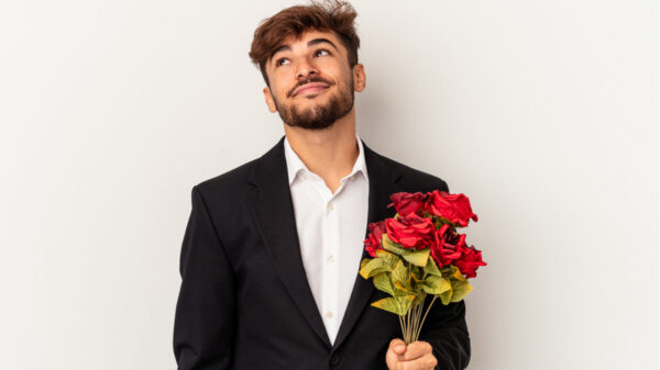 homem vestindo terno e segurando um buquê de rosas vermelhas em fundo claro