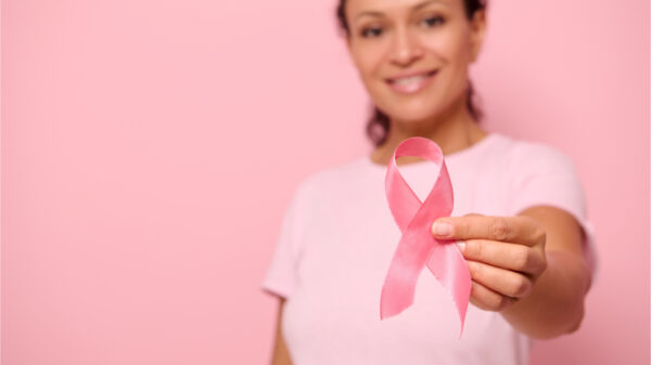 Mulher sorridente de camiseta rosa segurando uma fita de cetim na mão. Conscientização do câncer de mama, outubro rosa, fundo colorido. Conceito de apoio ao câncer de mama.