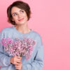mulher segurando flores em fundo rosa