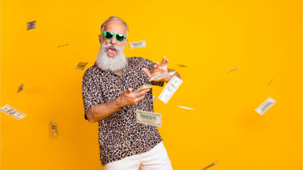 Retrato de homem engraçado, velho, barbudo e milionário de óculos desperdiçando dinheiro, jogarndo notas, usando shorts e camisa de leopardo, isolado sobre fundo amarelo.