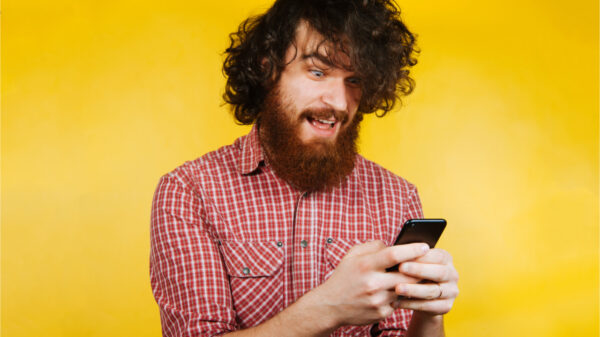 Jovem barbudo surpreso usando celular. Homem de barba surpreso. Homem com cabelo encaracolado e barba.