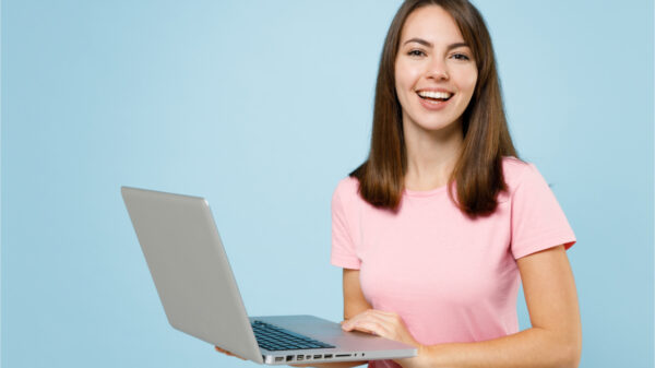 Mulher jovem sorridente, feliz em blusa rosa usando computador portátil, isolada no retrato de estúdio de fundo azul claro pastel. Conceito de estilo de vida de pessoas.
