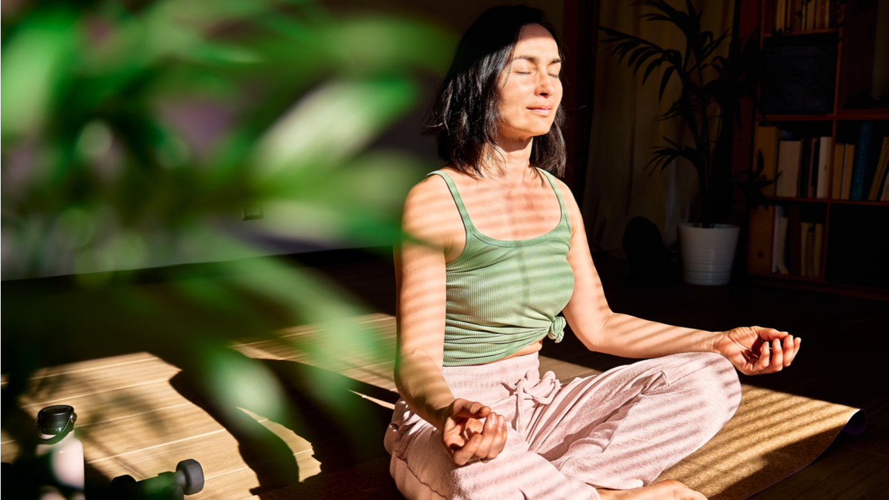 mulher usando blusa verde e fazendo meditação em um ambiente iluminado em com plantas