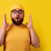 Homem de óculos surpreso sobre fundo amarelo.