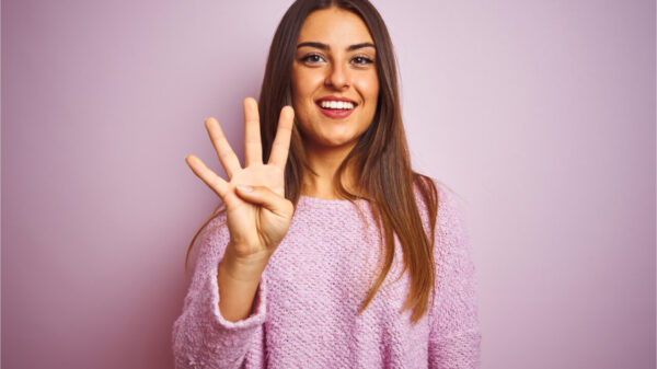 Mulher jovem vestindo suéter casual, de pé sobre fundo rosa, isolada, mostrando e apontando para cima com os dedos em número quatro enquanto sorri confiante e feliz.