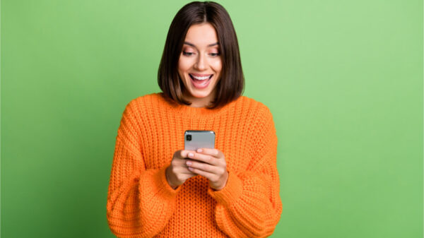 Retrato de uma garota alegre usando celular, isolada sobre fundo de cor verde.