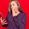 Mulher jovem usando tablet sobre fundo vermelho isolado, cobrindo a boca com a mão, chocada. Expressão surpresa.