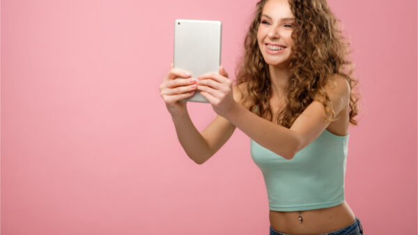 Garota de cabelo encaracolado tirando foto em tablet, isolada em fundo rosa.