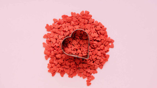 Punhado de corações de açúcar vermelhos e coração de metal no fundo rosa.