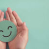 Mãos segurando um sorriso feliz verde. Saúde mental, bem-estar.