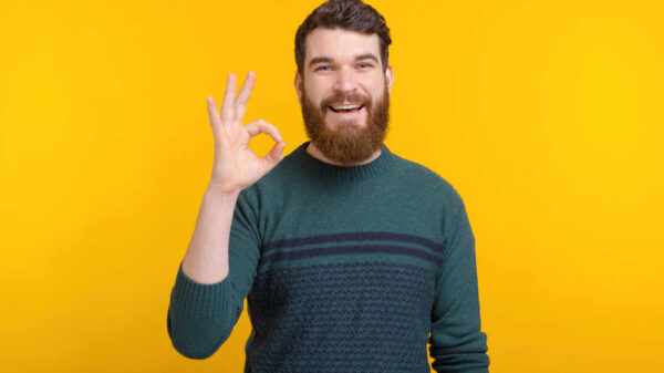 Retrato de um jovem fazendo gesto de "ok" sobre fundo amarelo.