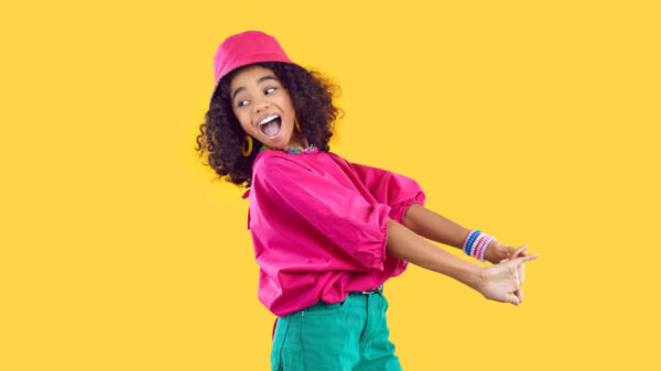 Adolescente alegre se divertindo em fundo amarelo vívido. Garota feliz e enérgica de roupas coloridas da moda se divertindo e brincando.