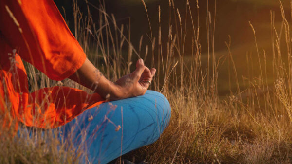 Pessoa em posição de lótus na natureza, nas montanhas, sentada na grama ao pôr do sol, meditando com mantras, gesto de mão zen.