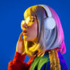 Retrato de uma mulher ouvindo música em fundo colorido.