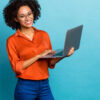 Retrato de uma mulher alegre de cabelos cacheados usando laptop, isolada em fundo de cor azul.