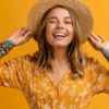 Mulher elegante em vestido amarelo e chapéu de palha posando em fundo amarelo, isolada, com expressão sorridente no rosto, feliz, com dentes brancos. Tendência de estilo de moda de verão.