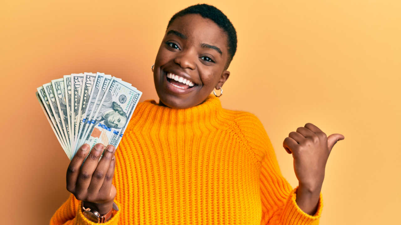 mulher negra segurando dinheiro em fundo amarelo