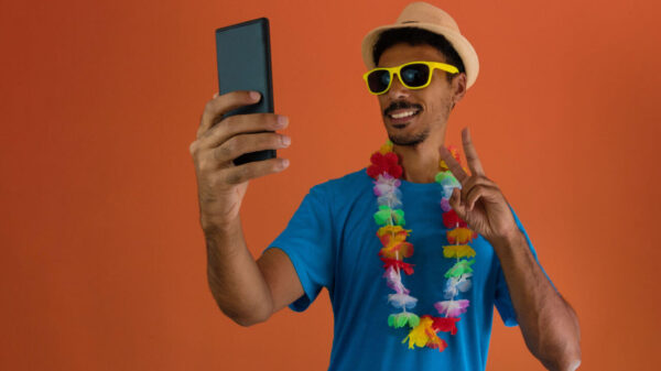 Homem fantasiado para o carnaval do Brasil, segurando celular, isolado em fundo laranja.