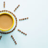 Caneca amarela de café com leite na mesa azul pastel clara de cima. Sol criado a partir de sementes de café marrons. Vista superior.