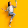 Retrato em tamanho real de uma mulher segurando um telefone, de bom humor, isolada em um fundo de cor amarela.