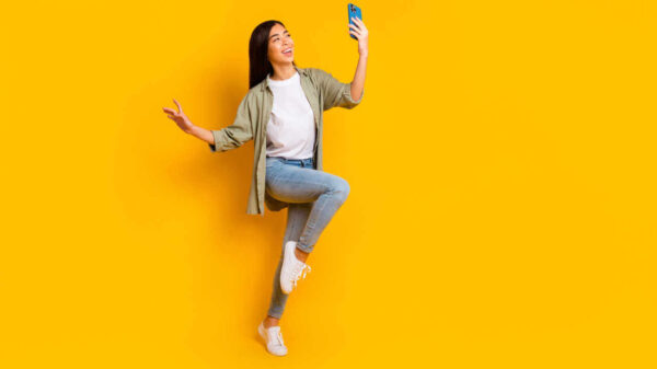 Retrato em tamanho real de uma mulher segurando um telefone, de bom humor, isolada em um fundo de cor amarela.