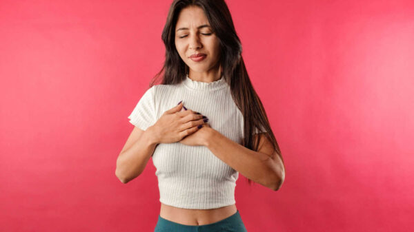 Jovem mulher isolada sobre fundo vermelho, sofrendo, com as mãos no peito.