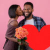 Homem segurando coração vermelho, e mulher com buquê de rosas beijando-o no fundo do estúdio rosa.
