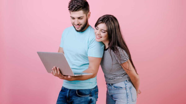 Casal jovem de homem e mulher olhando no laptop, isolados sobre fundo rosa.