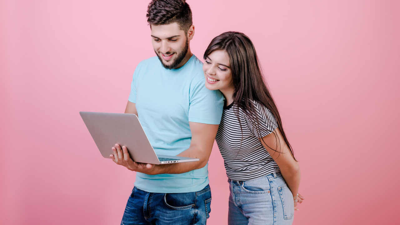 Casal jovem de homem e mulher olhando no laptop, isolados sobre fundo rosa.