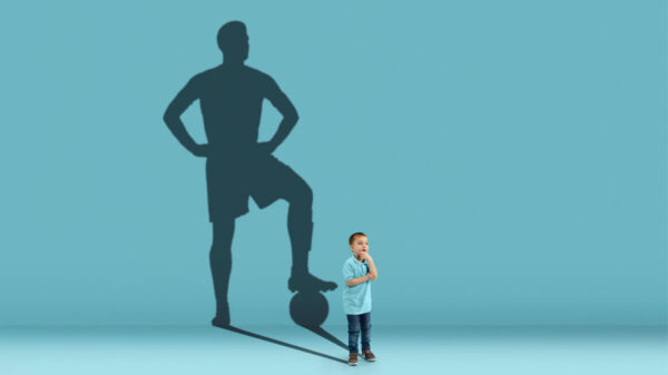 Conceito de infância e de sonho. Imagem conceitual de menino e de uma sombra de um jogador de futebol, em fundo azul.