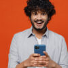 Homem sorrindo, segurando um celular, sobre fundo vermelho.