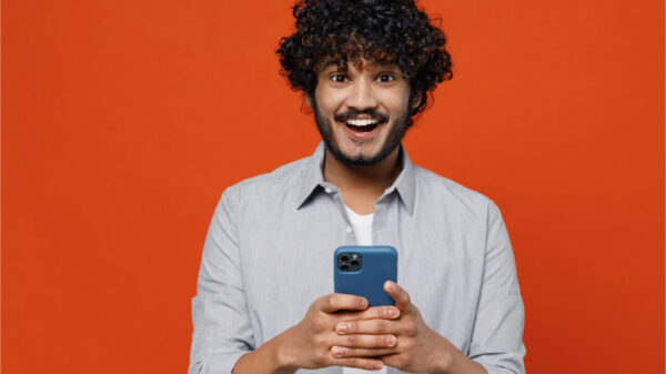 Homem sorrindo, segurando um celular, sobre fundo vermelho.