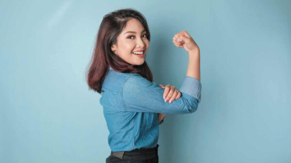 Mulher vestindo uma camisa azul, fazendo um gesto de força, levantando o braço e mostrando o músculo, sorrindo com orgulho.