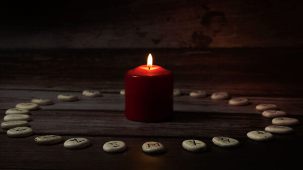 Pedras rúnicas com símbolos pretos para adivinhação em círculo com uma vela no meio sobre uma mesa de madeira.