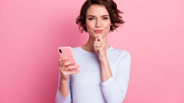 Retrato de uma mulher usa um smartphone, isolada sobre um fundo de cor rosa pastel.