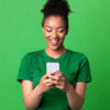 Retrato de mulher feliz, usando smartphone, contra uma parede verde de um estúdio.