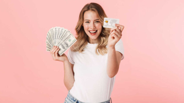 mulher com roupa branca segurando dinheiro e cartão de crédito em fundo rosa